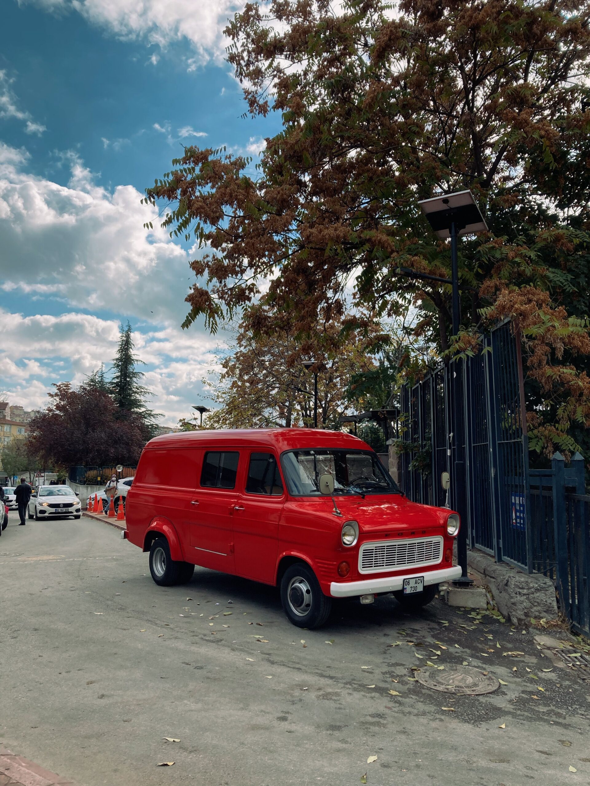 A vibrant red vintage van parked on a leafy street under a clear sky.