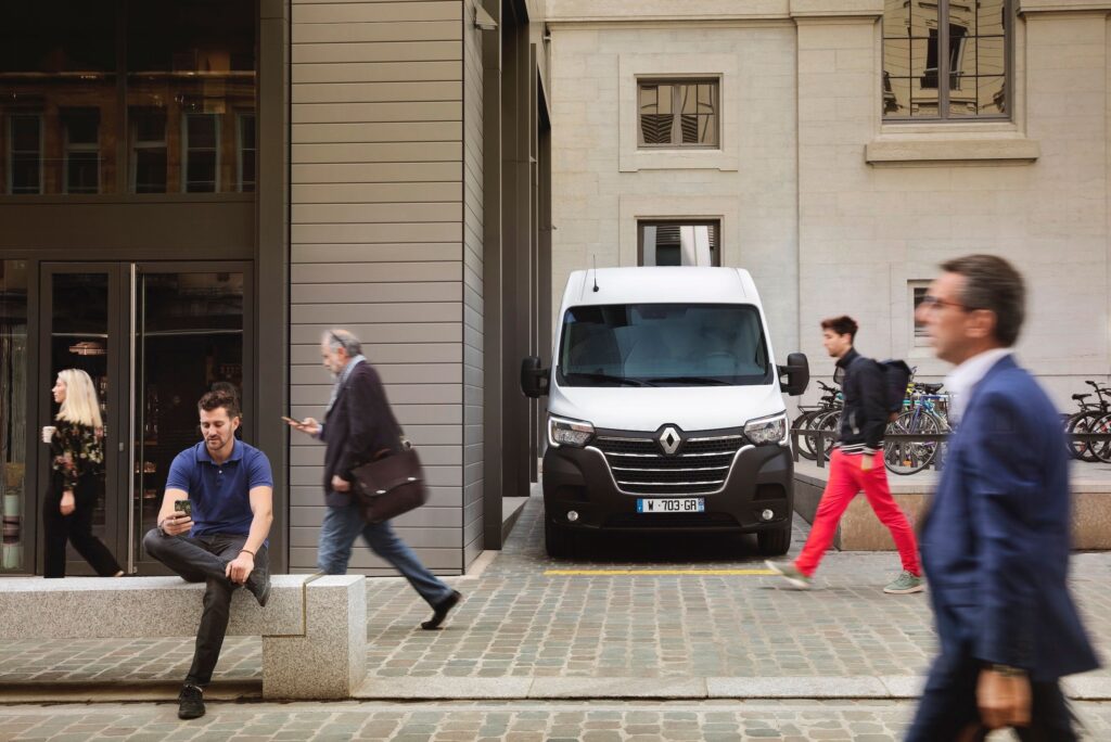 Lively street view in a Belgian city featuring pedestrians and a parked van.