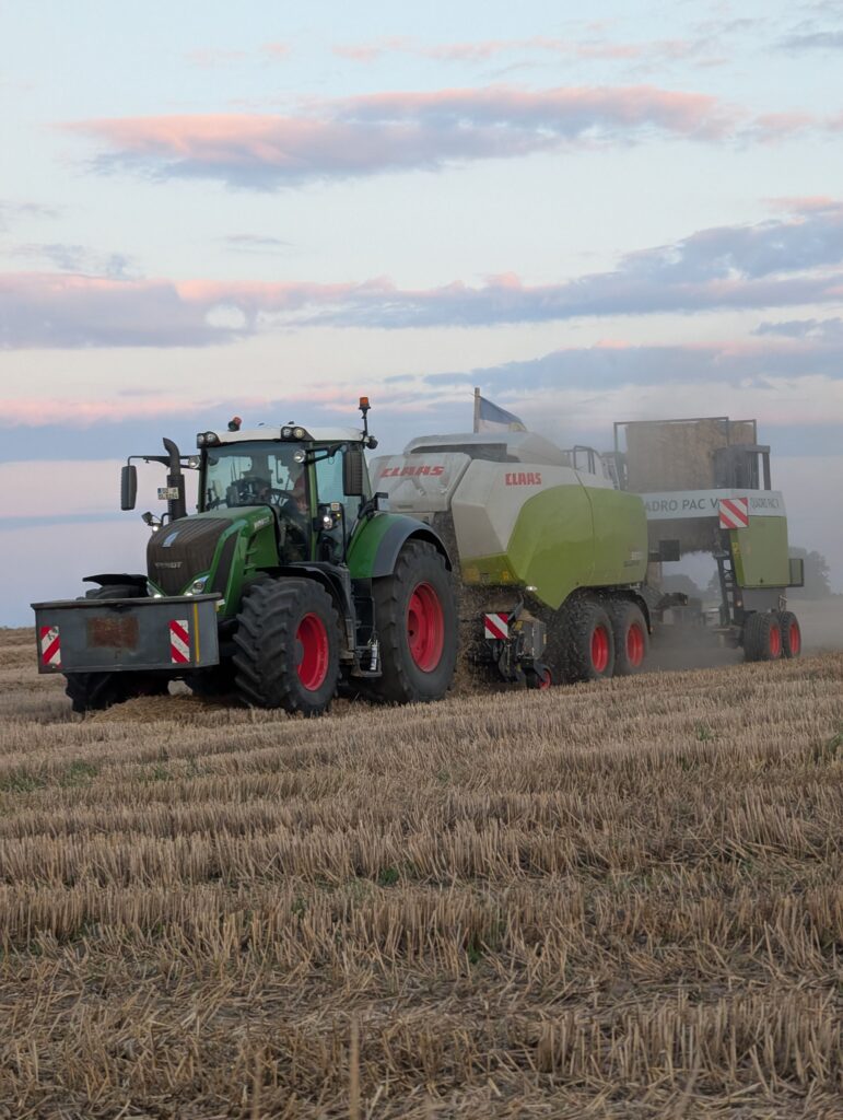 Tractor and combine harvester working in a field during sunset, showcasing agricultural machinery.