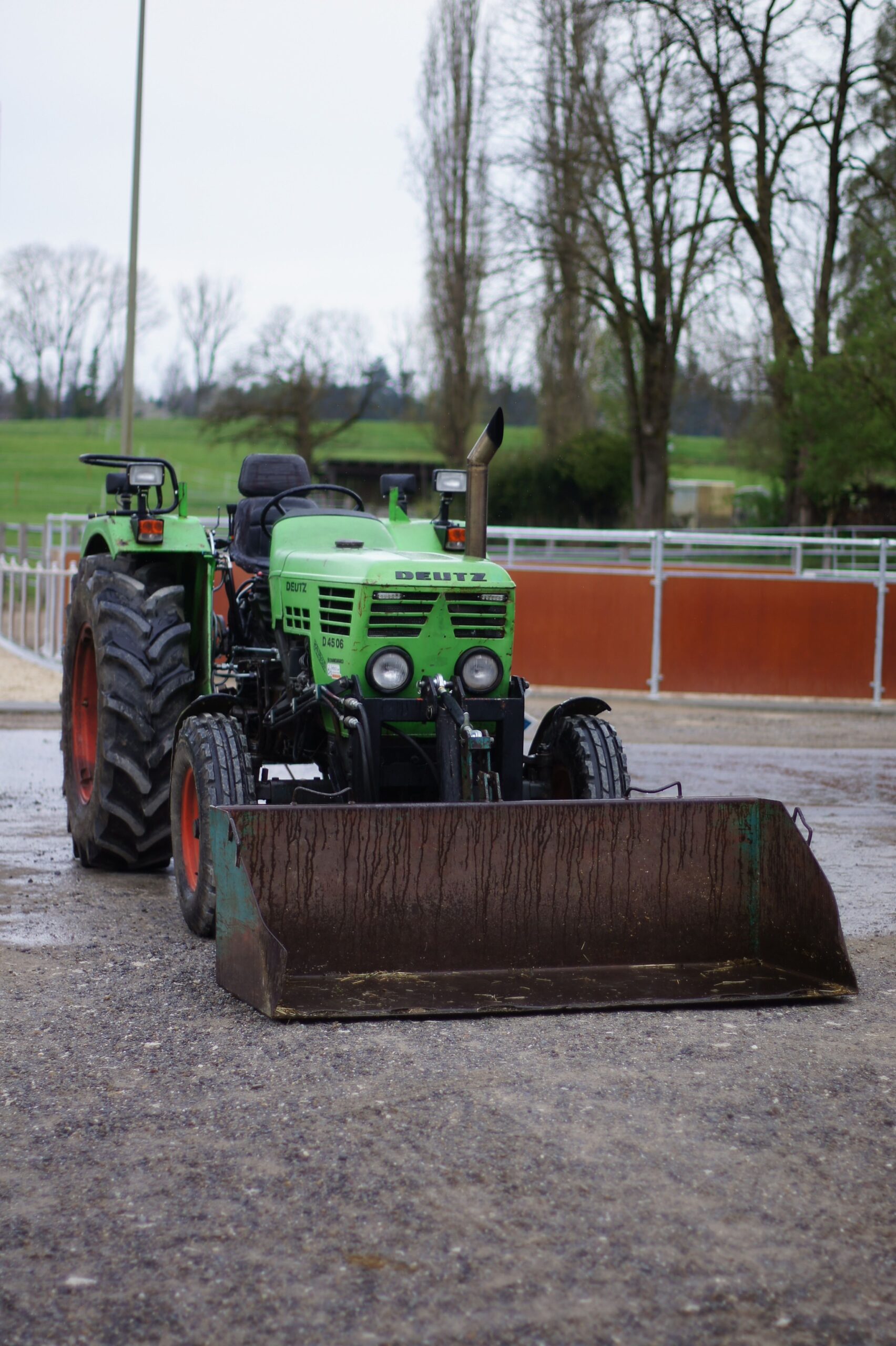 A vibrant green tractor parked outdoors in a Swiss farm environment during a cloudy day.